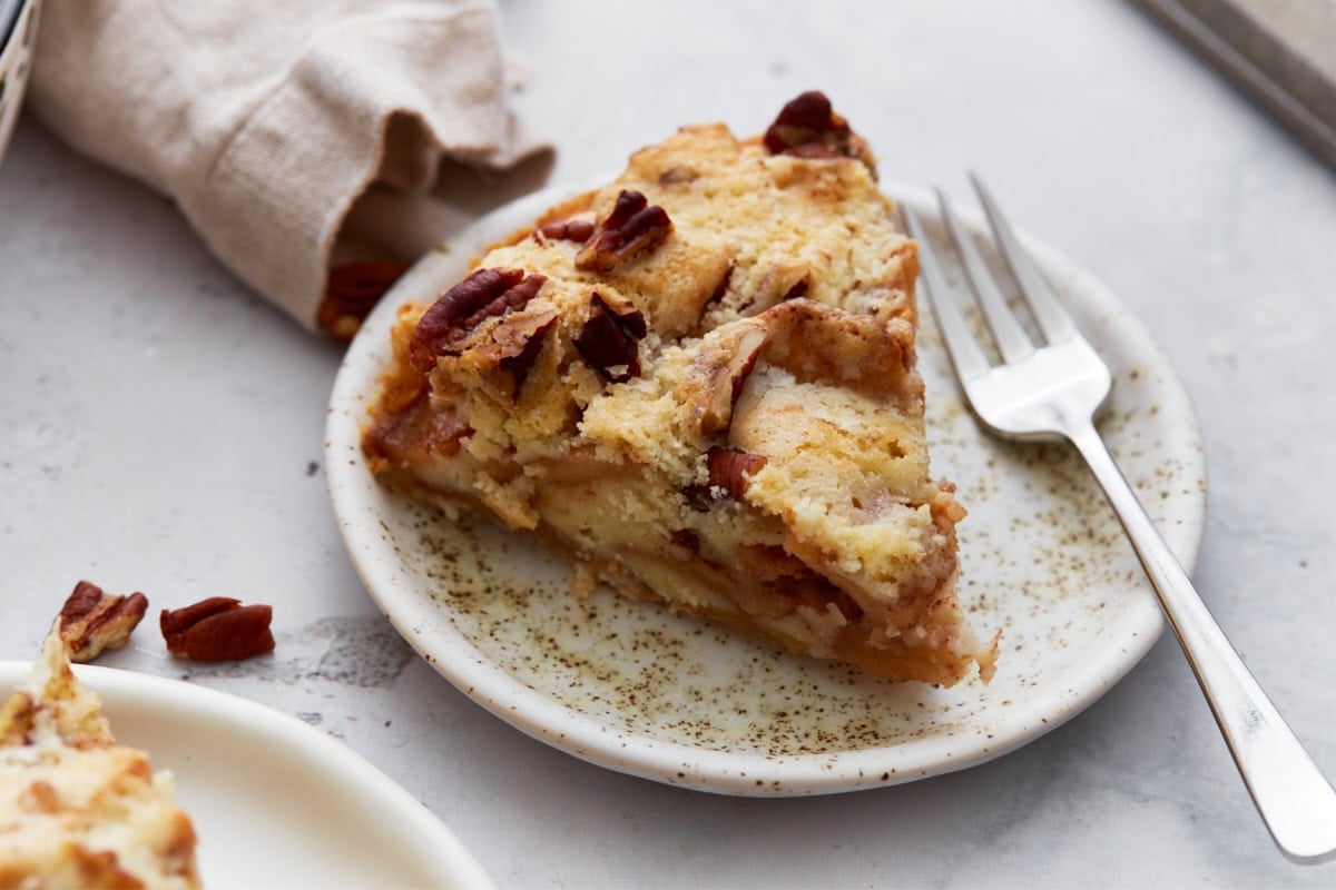 Slice of crustless apple pie on a small speckled plate with a fork, showing tender apples and a crumbly topping.