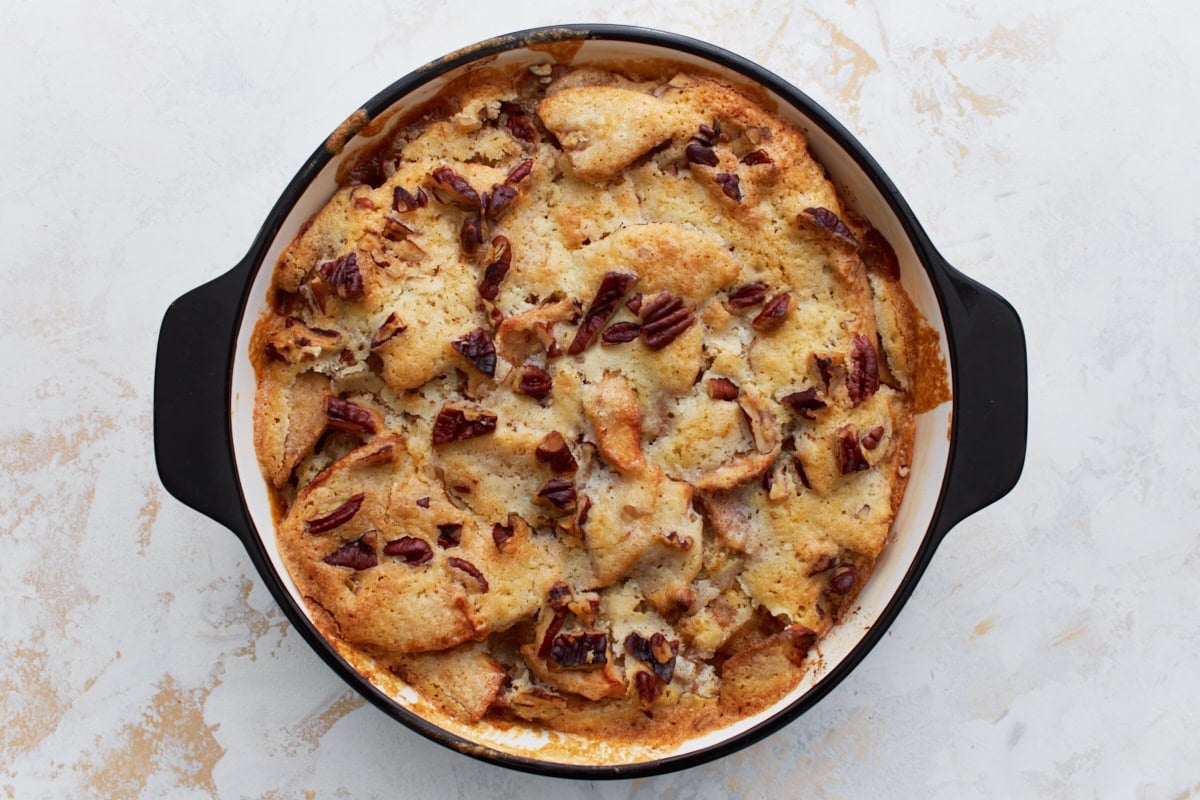 Freshly baked crustless apple pie with a golden-brown top and toasted pecans, still in the round baking dish.