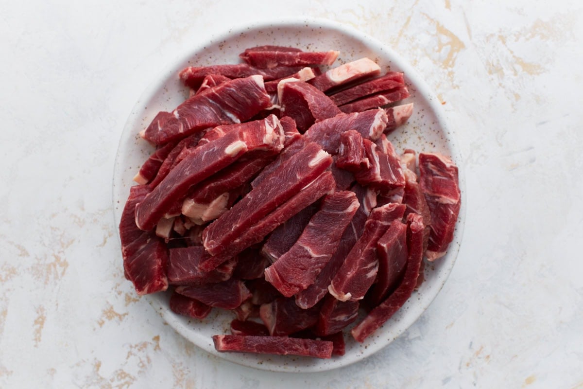 Plate of thinly sliced raw beef sirloin, ready for searing.