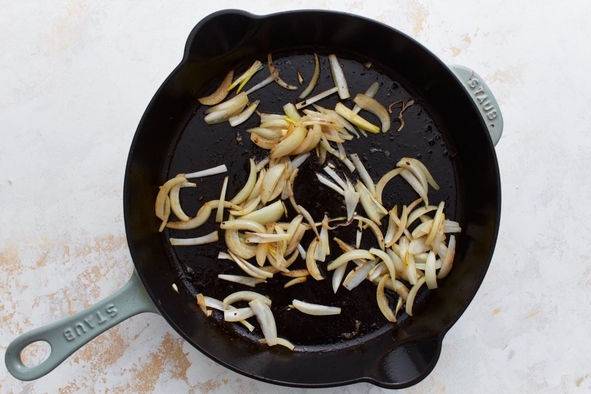 Sliced onions sautéing in the same skillet after the beef has been removed.