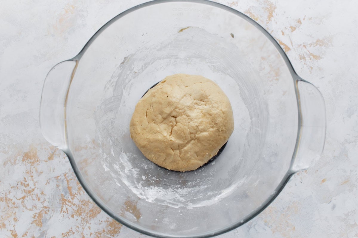 Beignet dough after kneading, formed into a rough ball in a glass mixing bowl.