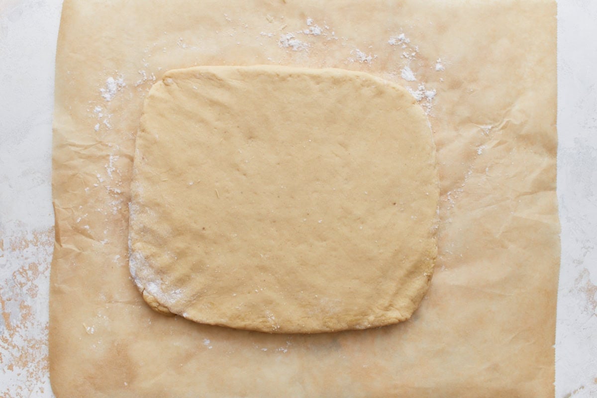 Rolled-out beignet dough on parchment paper, dusted lightly with flour.