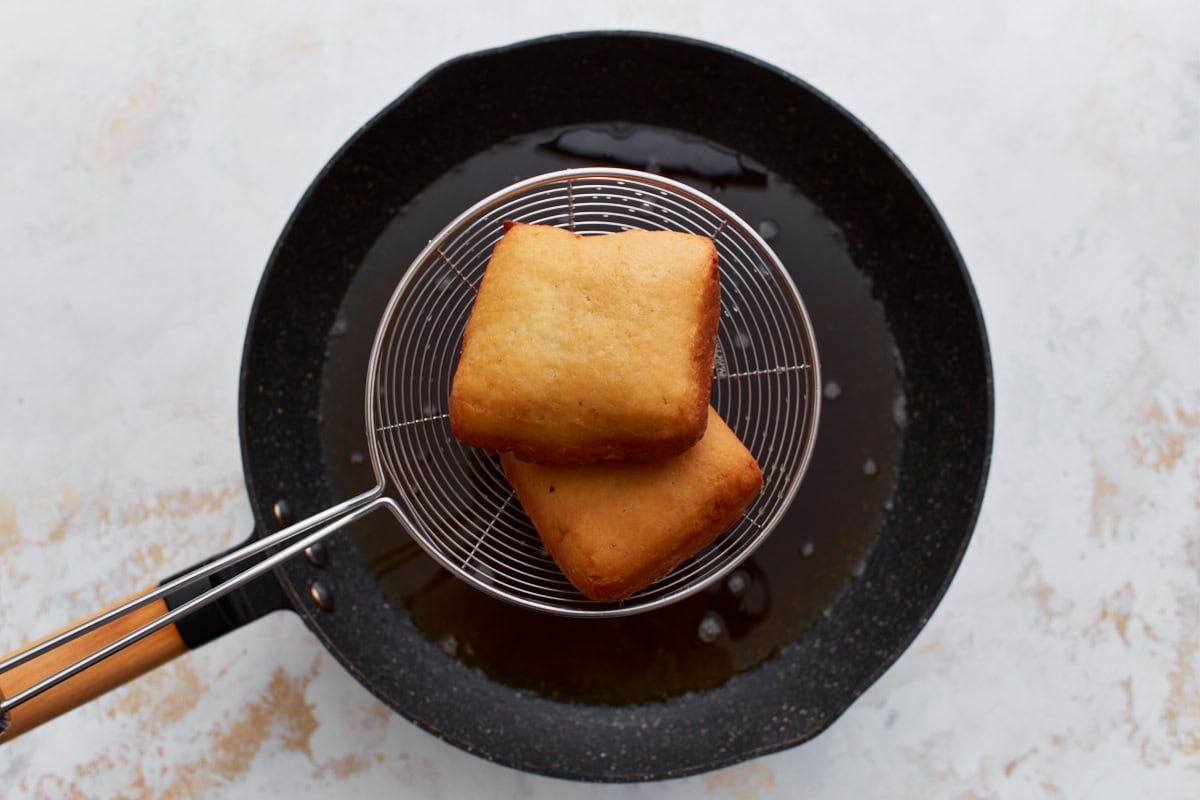 Fried gluten-free beignets lifted from hot oil with a wire strainer, golden and crisp.