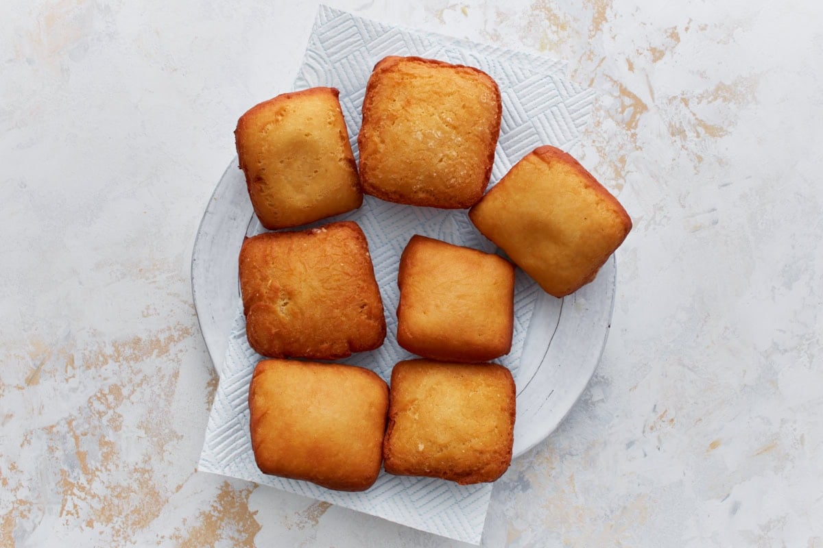 Freshly fried beignets resting on a paper towel–lined plate to drain excess oil.