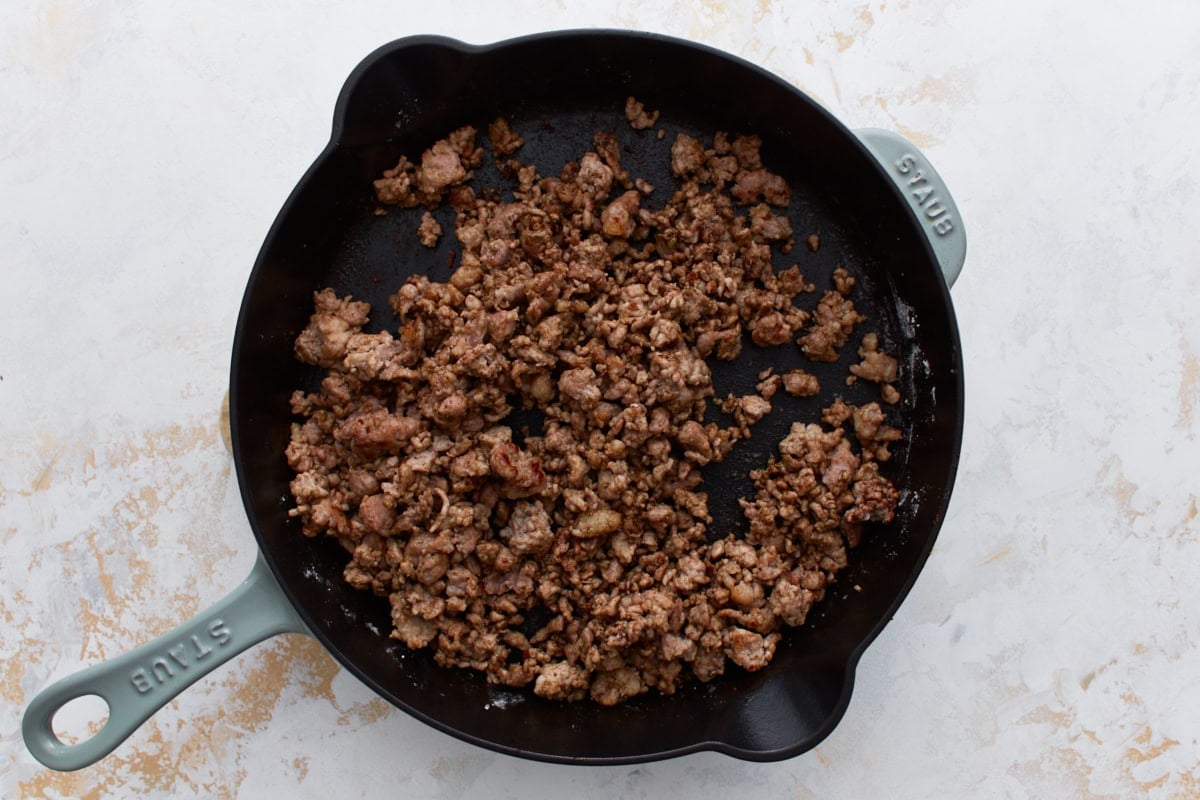 Sausage in a skillet mixed with flour and spices, forming the base for gluten-free gravy.