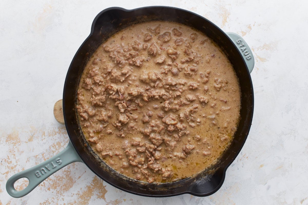 Sausage gravy simmering in a cast iron skillet, starting to thicken as it cooks.