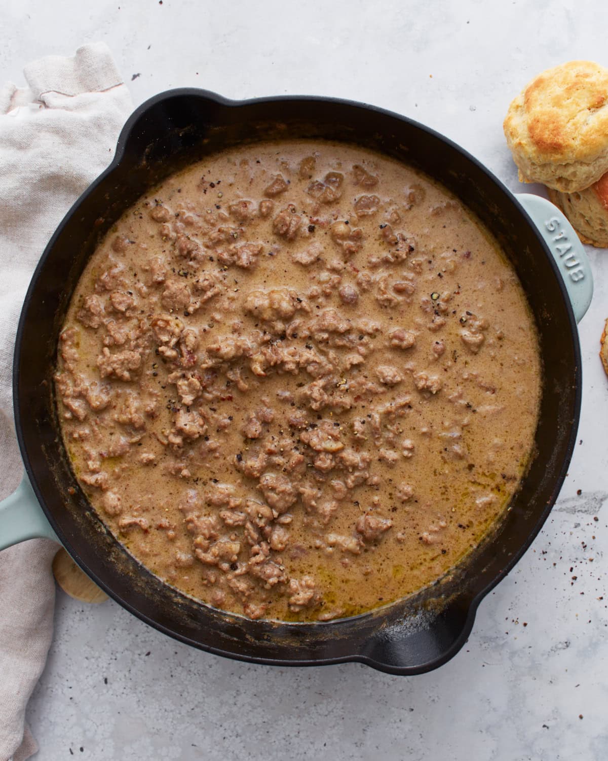 Overhead view of a cast iron skillet filled with thick, creamy gluten-free sausage gravy, with golden biscuits on the side.