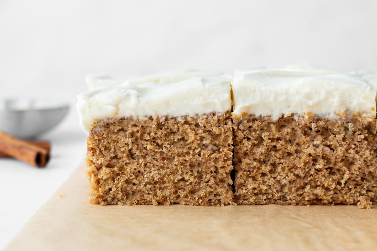 Close-up side view of a slice of gluten-free spice cake with thick cream cheese frosting, showing moist crumb and texture.