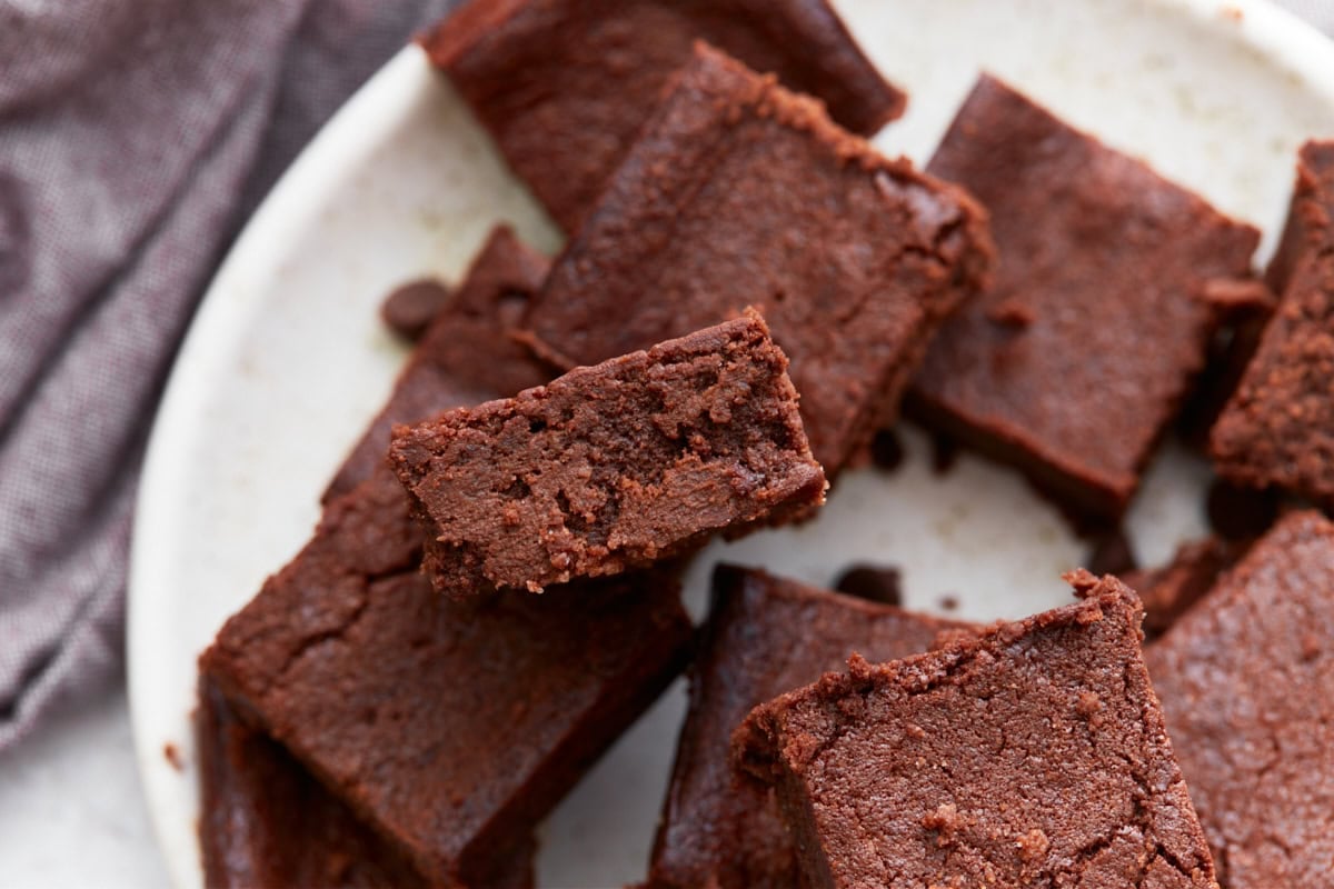 Overhead view of several keto brownies on a plate, with one brownie angled to show its moist, dense crumb.