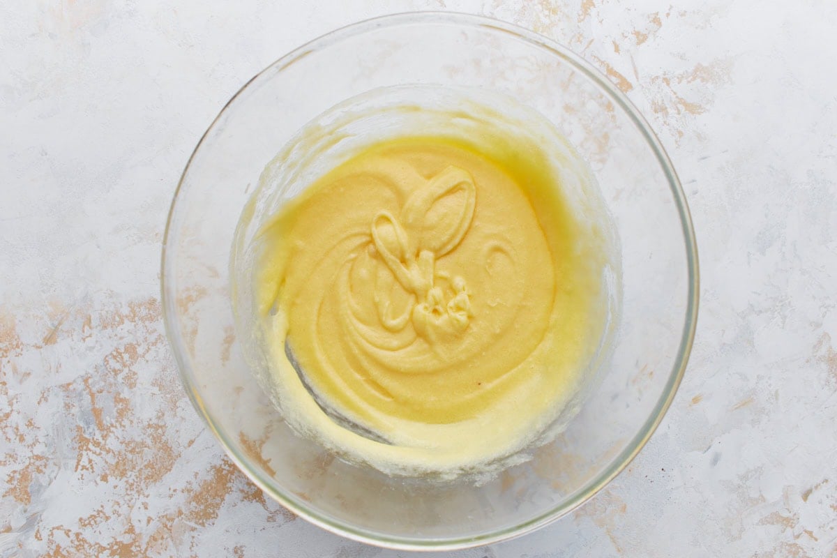 A glass bowl showing a creamy, pale yellow batter after eggs and vanilla have been added to the butter and sweetener mixture.