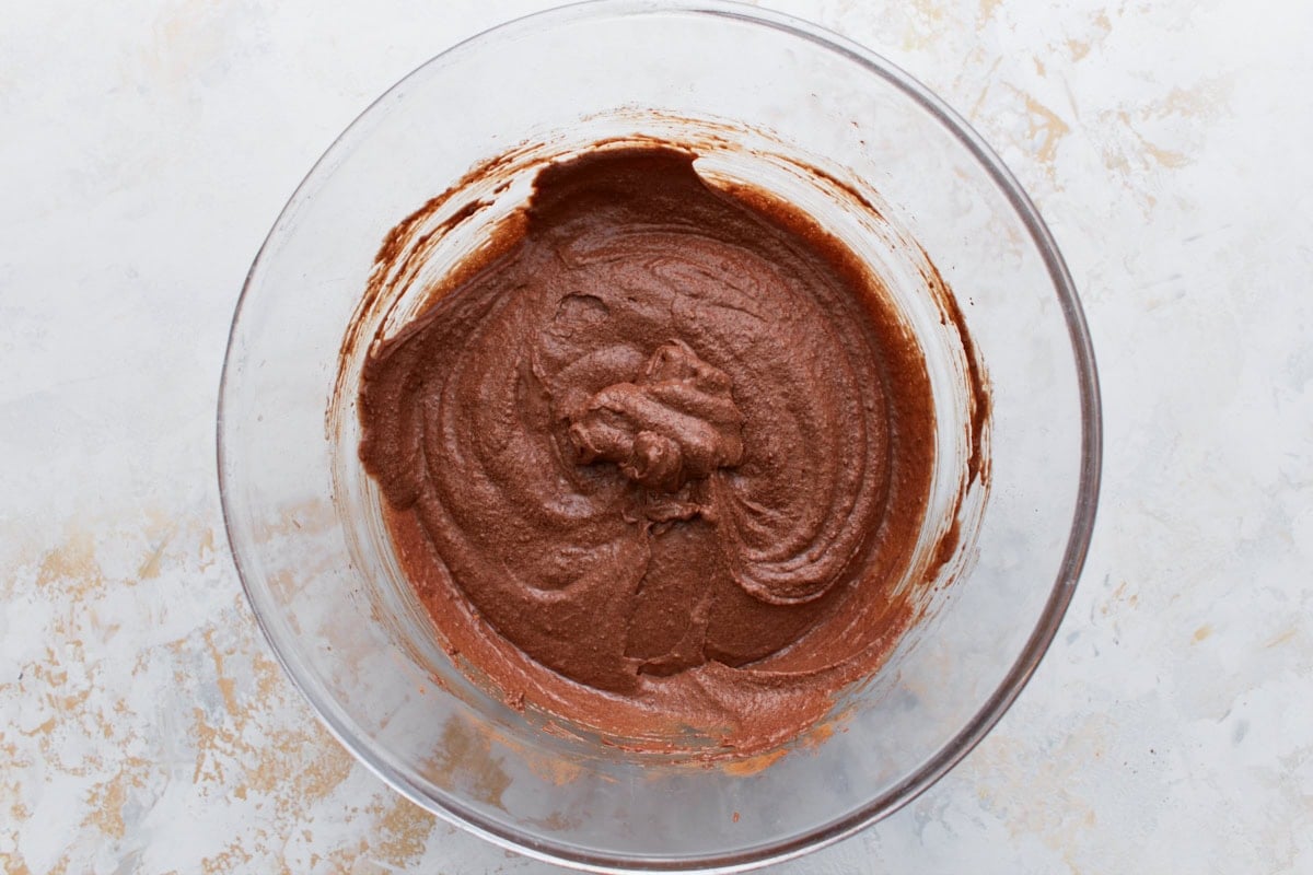 A glass bowl filled with thick chocolate brownie batter made with almond flour and cocoa powder.