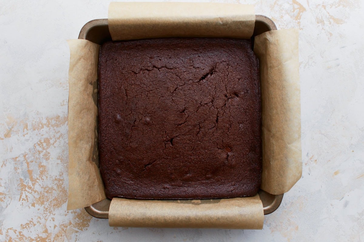 Freshly baked keto brownies in a parchment-lined pan, with a smooth, cracked top indicating a fudgy center.