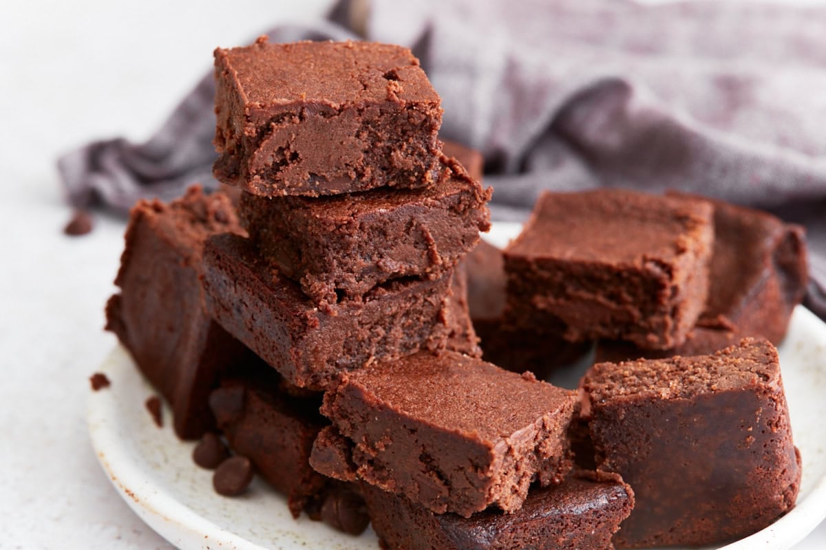 A plate of cut keto brownies stacked in a rustic pile, with rich chocolate color and soft interiors visible.