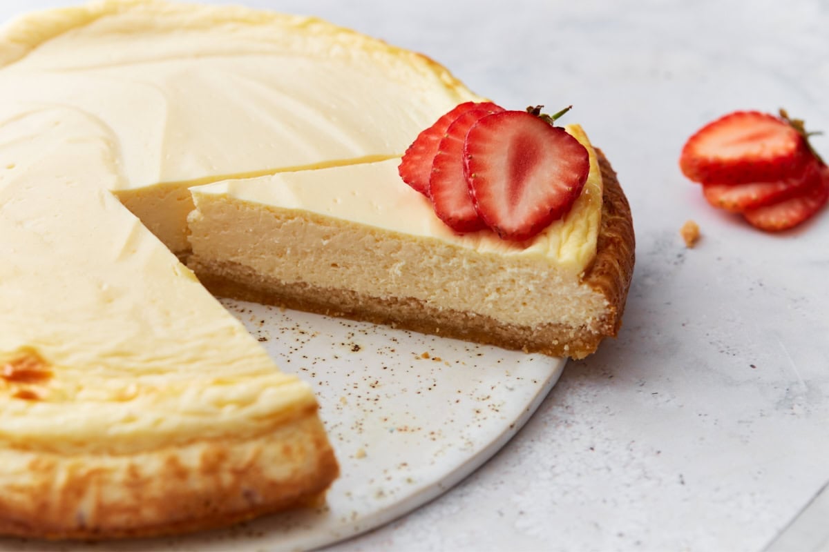 Close-up of a sliced keto cheesecake with one piece slightly lifted and topped with fresh strawberry slices.