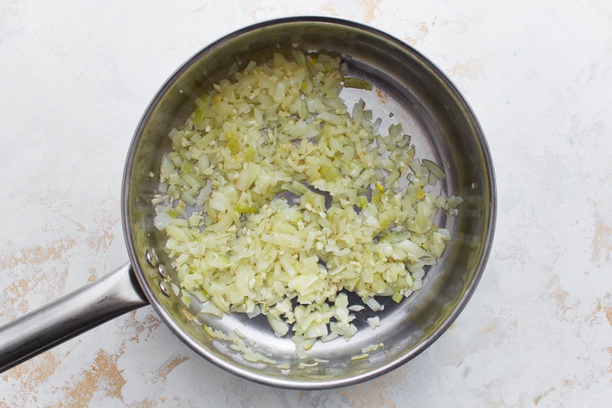 Finely chopped onions and minced garlic sautéing in a stainless steel skillet until soft and translucent.