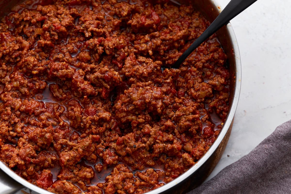 A close-up view of thick, hearty keto chili in a skillet, with visible chunks of meat and tomato in a rich sauce.