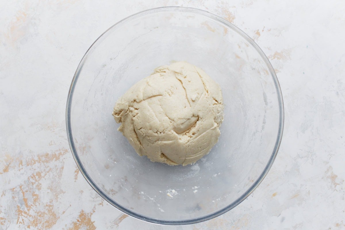 A clear mixing bowl filled with a ball of smooth, hydrated masa dough on a light-colored countertop.