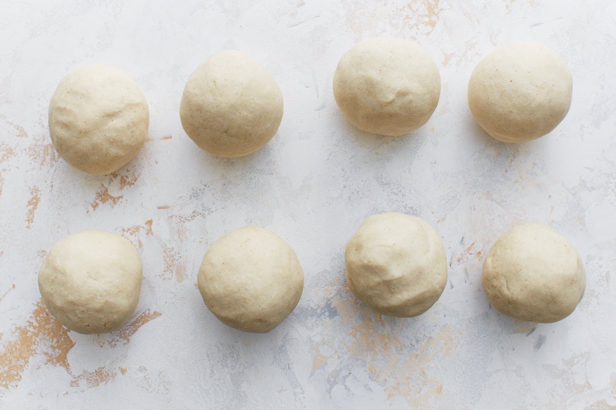 Eight evenly portioned dough balls arranged on a light surface, ready to be shaped into pupusas.