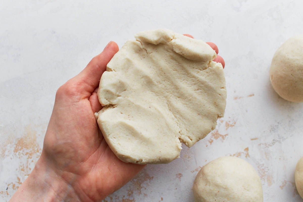 A hand holding a flattened disc of masa dough, showing the soft texture ready for filling.