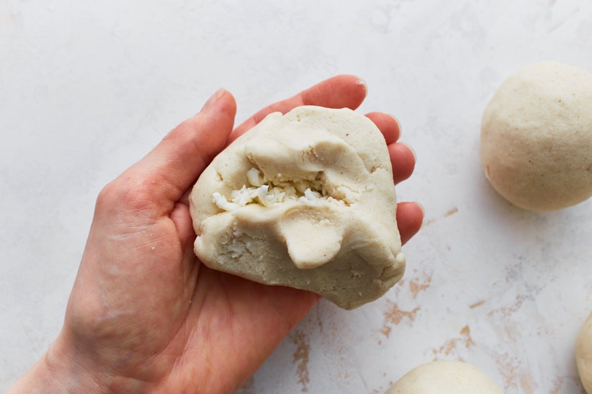 Masa dough being folded over cheese filling in a hand, showing the pupusa being sealed.