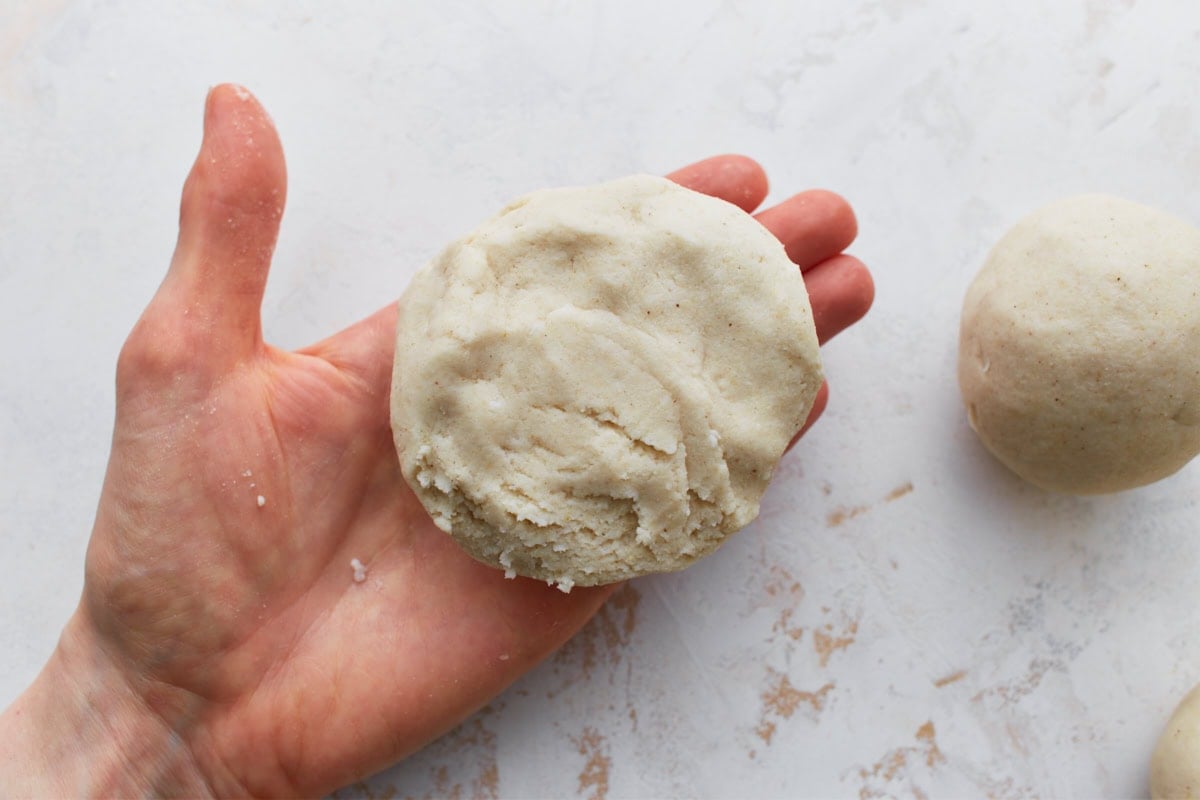 A sealed and flattened pupusa held in a hand, ready to be cooked.