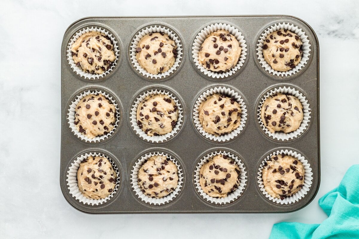 Overhead view of a muffin tray filled with chocolate chip muffin batter in paper liners, ready to bake.