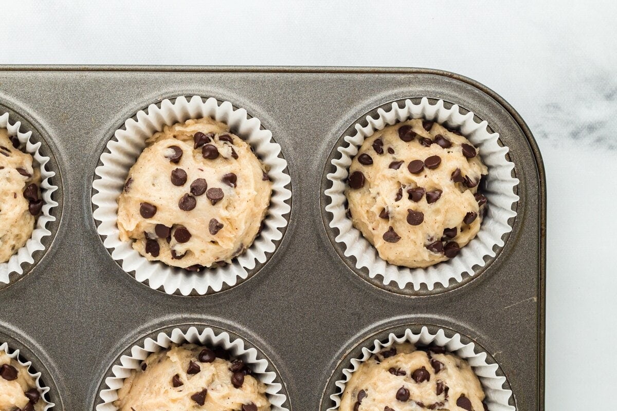 Close-up of unbaked muffin batter topped with chocolate chips in a lined muffin tin.