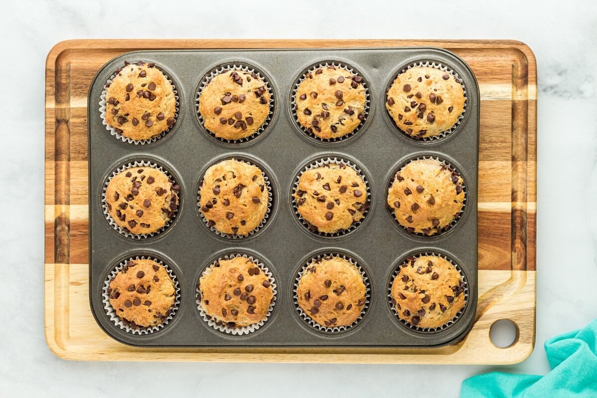Freshly baked gluten-free chocolate chip muffins still in the muffin tin, resting on a wooden cutting board.