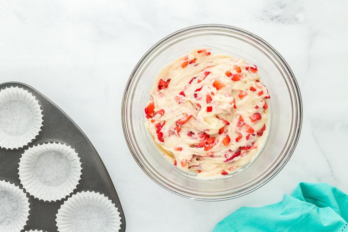 Strawberry muffin batter fully mixed in a large glass bowl, showing even distribution of chopped strawberries