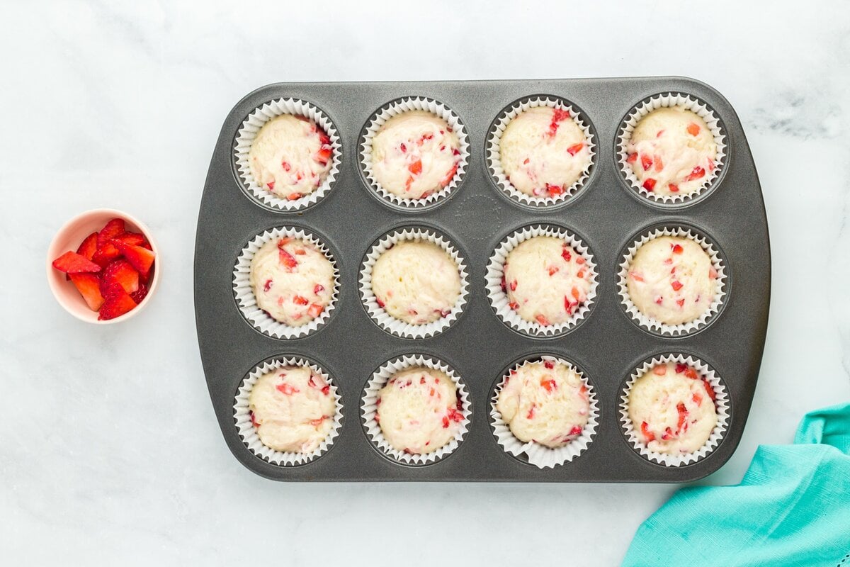 Muffin pan filled with strawberry muffin batter, each cup about three-quarters full and ready to bake