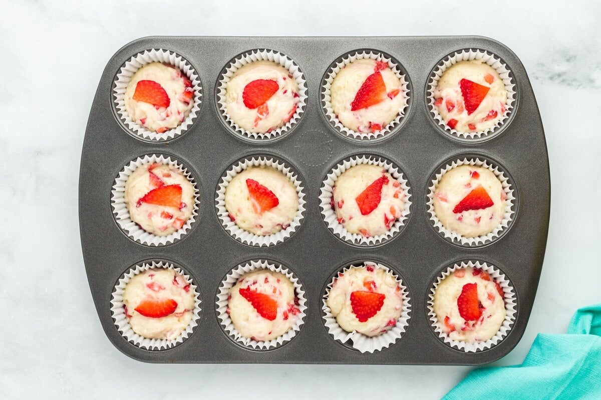 Muffin tin filled with batter topped with thin slices of strawberry for decoration before baking.