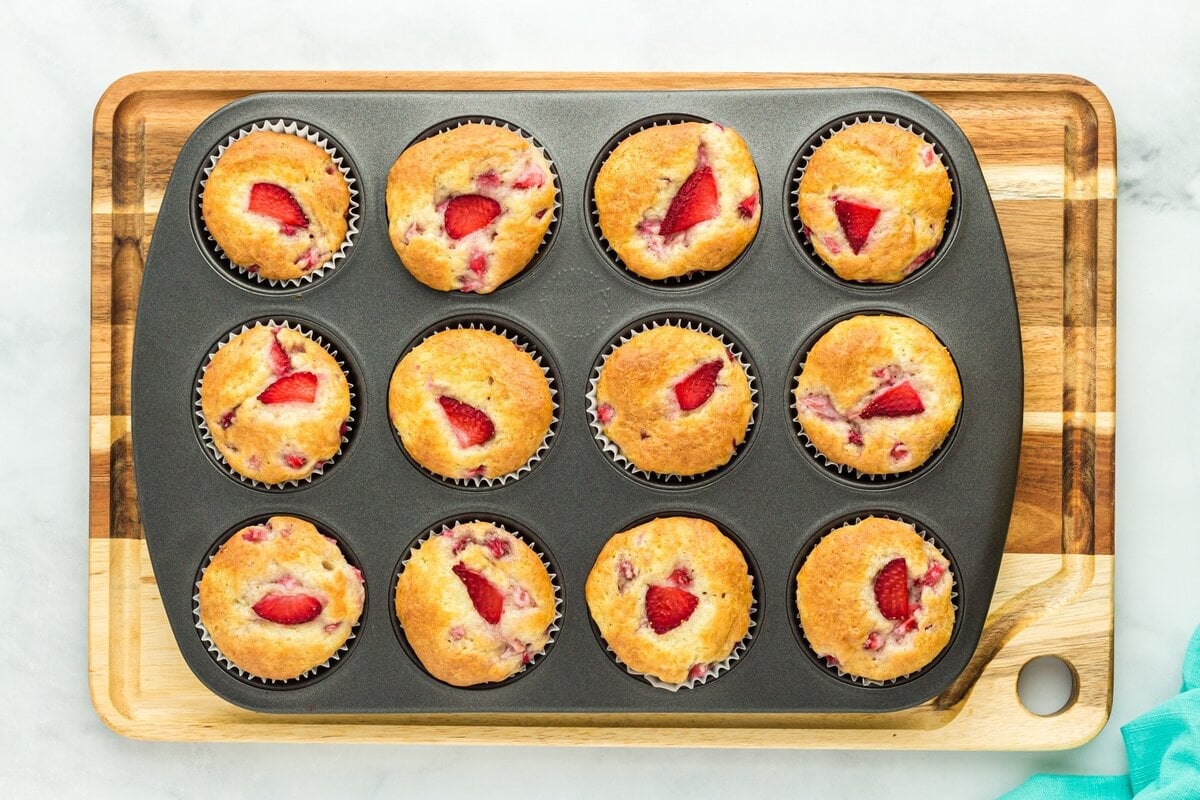 Freshly baked gluten-free strawberry muffins cooling in the muffin tin, tops golden brown with visible strawberry slices