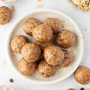 A plate of gluten free protein balls stacked in the center, surrounded by small bowls of chocolate chips, rolled oats, and chia seeds.