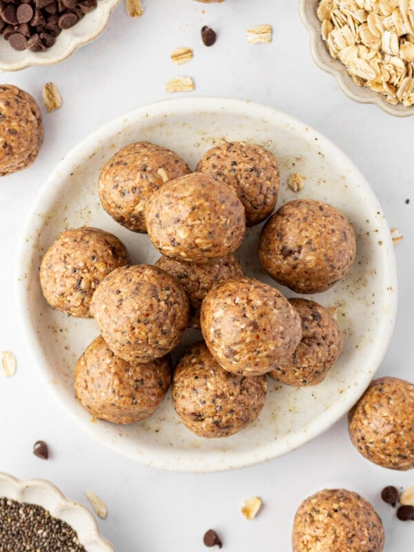 A plate of gluten free protein balls stacked in the center, surrounded by small bowls of chocolate chips, rolled oats, and chia seeds.