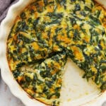 Baked crustless spinach quiche in a white pie dish with one slice removed.