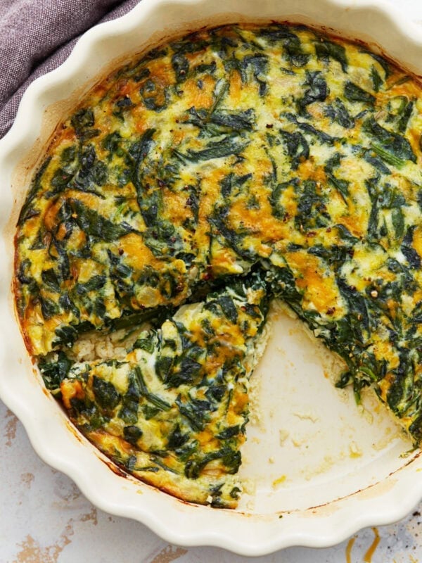 Baked crustless spinach quiche in a white pie dish with one slice removed.