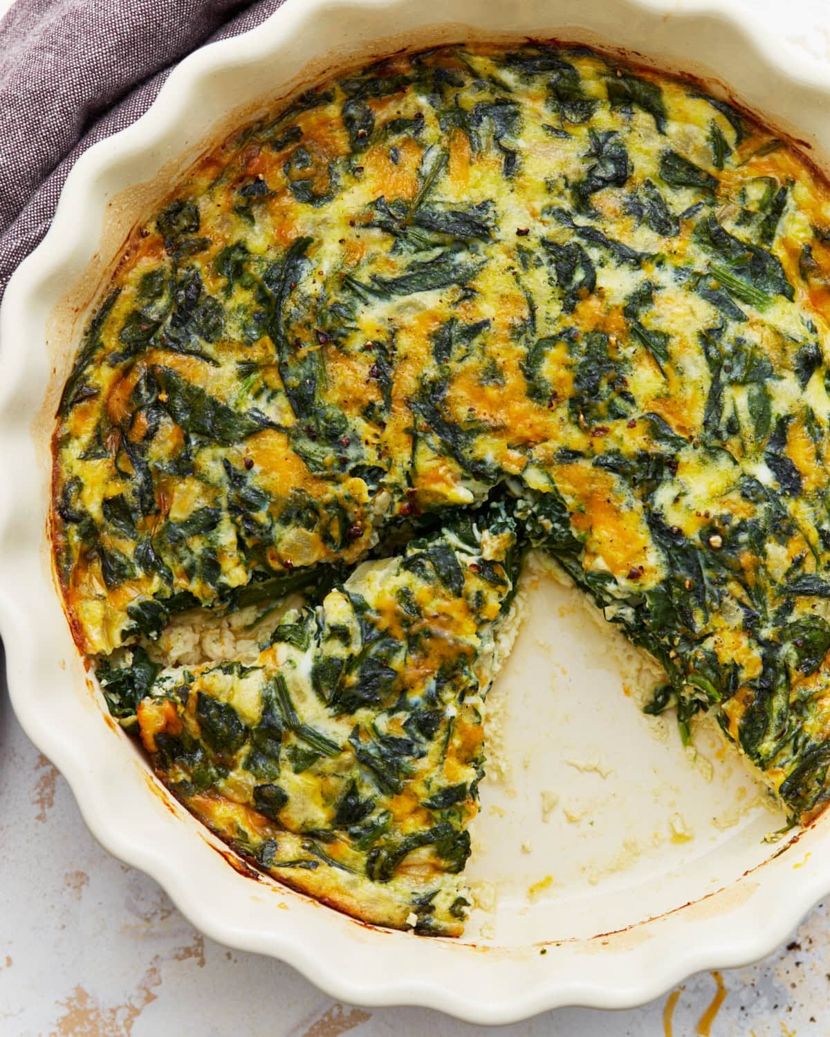 Baked crustless spinach quiche in a white pie dish with one slice removed.