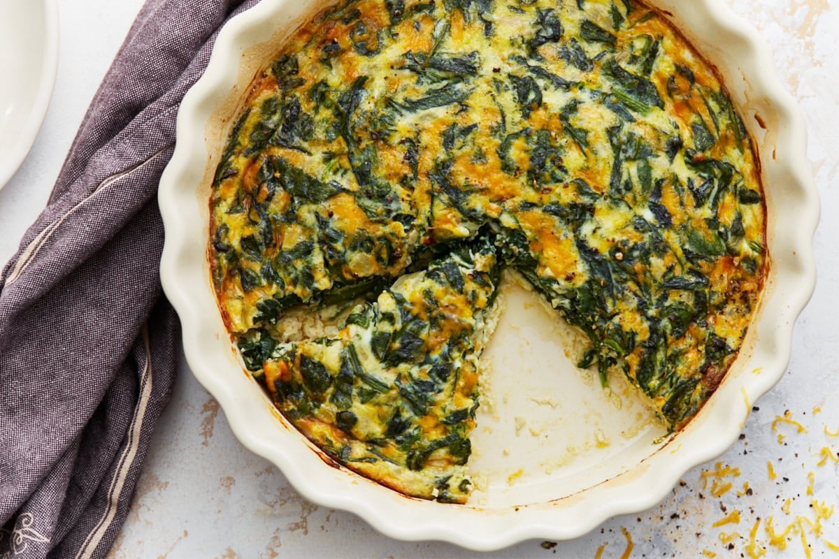 Crustless spinach quiche in a white pie dish with slices cut out.