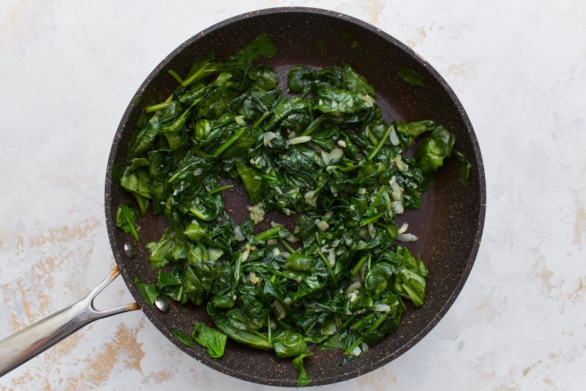 Fresh spinach cooking down with onions and garlic in a skillet.