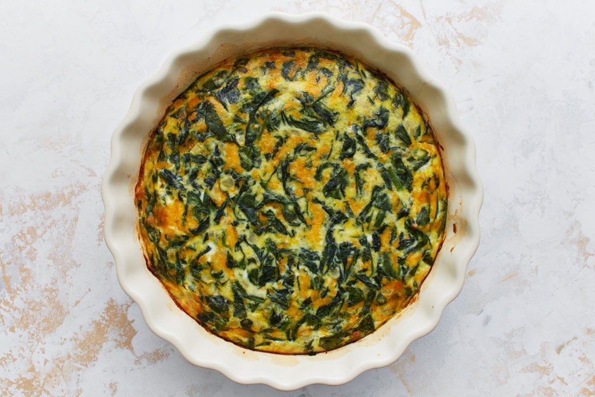 Golden baked crustless spinach quiche cooling in a pie dish.