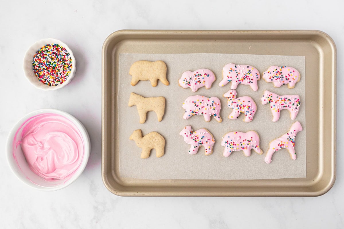 Baking sheet with undecorated and pink candy-coated gluten-free animal crackers, topped with rainbow sprinkles.