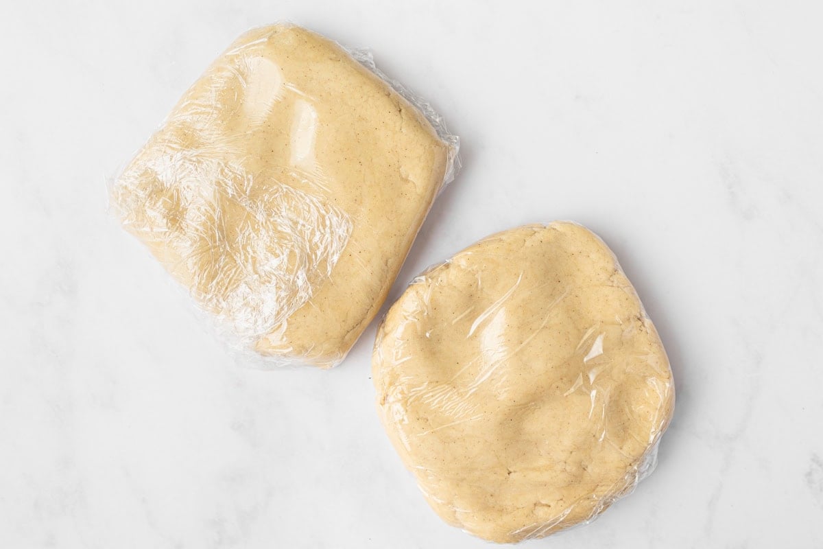 Two discs of gluten-free animal cracker dough wrapped in plastic wrap and ready to chill.