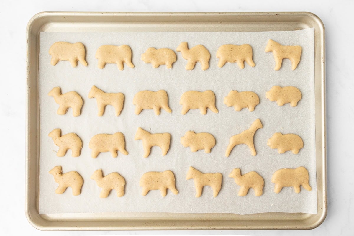 Unbaked gluten-free animal crackers arranged on a parchment-lined baking sheet, ready to go in the oven.