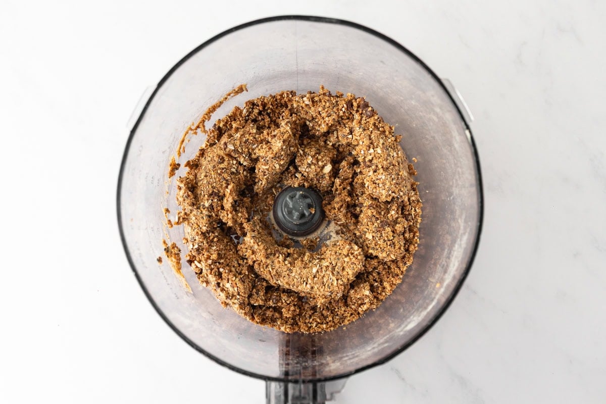 Overhead view of a food processor filled with a blended mixture of oats, nut butter, protein powder, and seeds for gluten free protein balls.