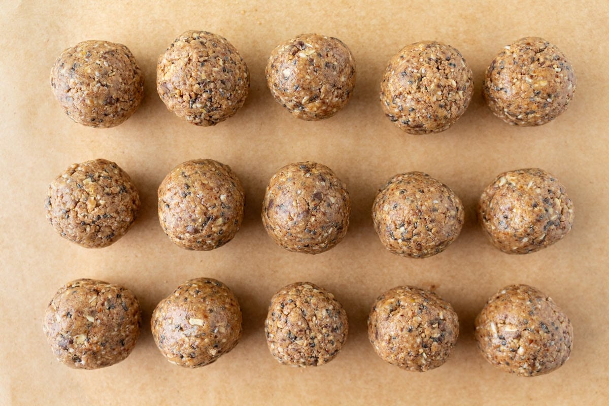 Rows of freshly rolled gluten free protein balls arranged neatly on a sheet of parchment paper.