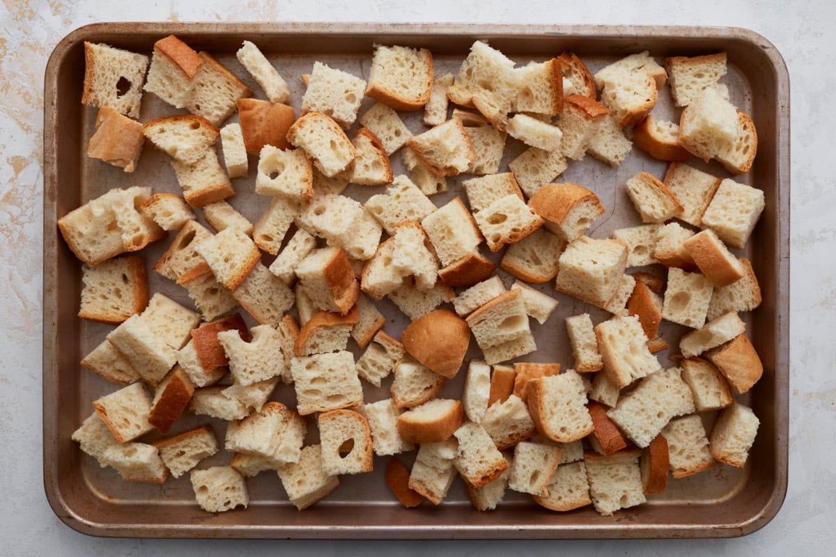 Freshly cut cubes of gluten-free bread spread out on a baking sheet, ready for toasting.