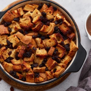 Golden baked gluten-free bread pudding topped with plump raisins, served in a round black-handled baking dish.