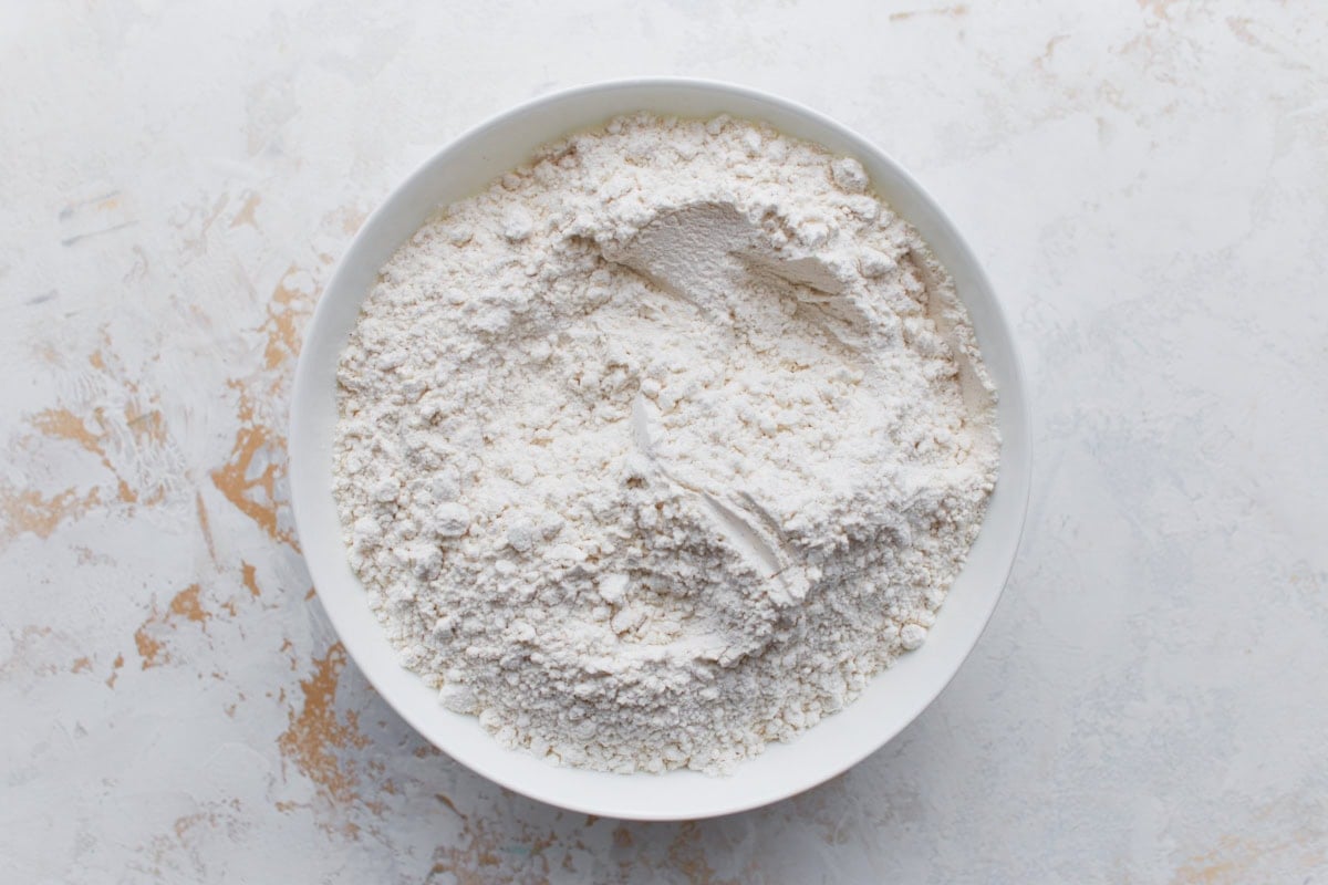 Overhead view of a white bowl filled with gluten-free all-purpose flour blend on a light textured surface.