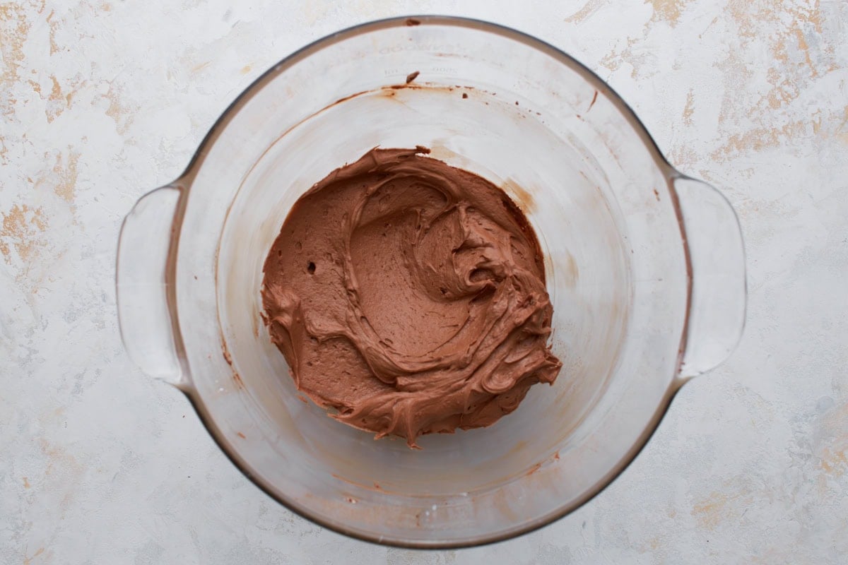 Light and fluffy chocolate buttercream frosting fully whipped in a glass mixing bowl.