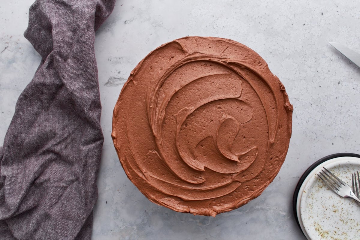 Overhead view of a round gluten-free yellow cake fully covered with swirls of chocolate buttercream frosting.
